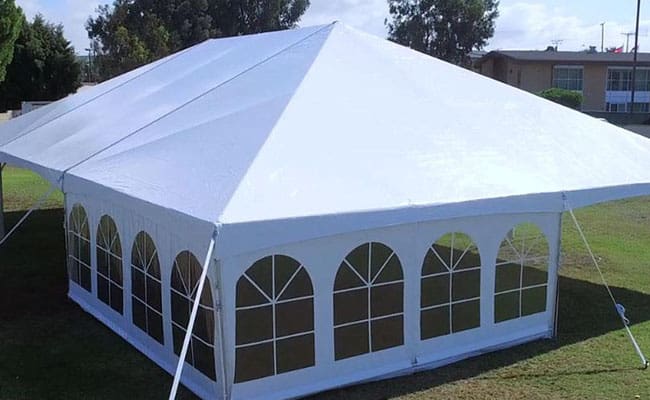 White outdoor event tent with arched windows set up on a grassy field, under a clear sky.