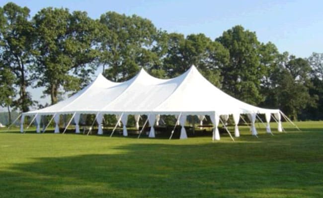 Large white event tent set up on a grassy field with trees in the background on a sunny day.