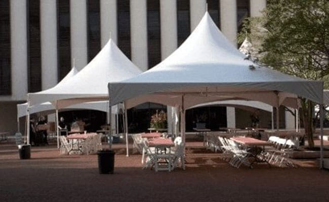 White tents set up in an outdoor plaza with scattered chairs and tables, near a building with vertical stripes.