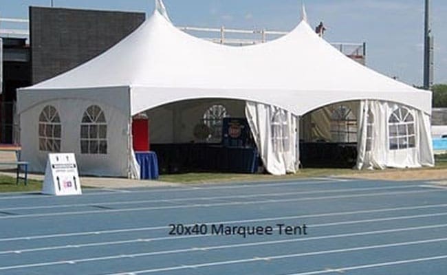 White marquee tent set up beside a running track, with open sides revealing tables and chairs inside, and a small sign placed in front.