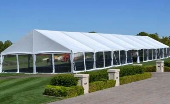 Large white outdoor event tent with clear sidewalls set up on a manicured lawn under a clear blue sky.