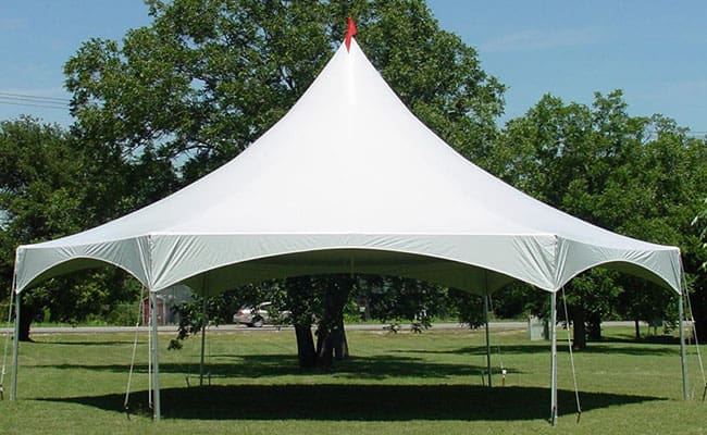 A large white canopy tent set up in a grassy park with trees in the background under a clear sky.