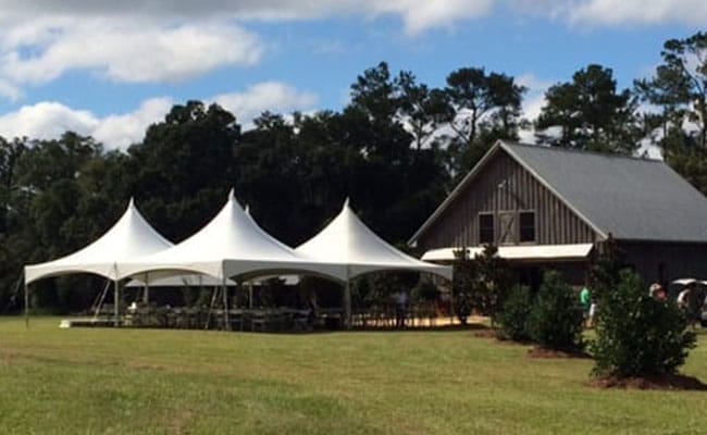 White event tents set up near a barn on a grassy field under a clear sky.