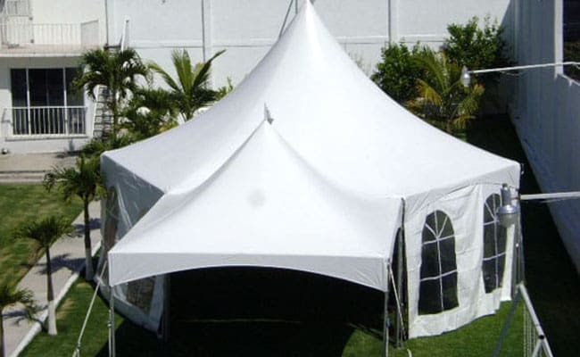 White canopy tent with sidewalls and windows set up on grass, surrounded by palm trees and a building in the background.