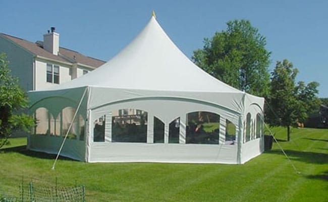 White event tent with open sides set up on a grassy field near a residential building on a sunny day.