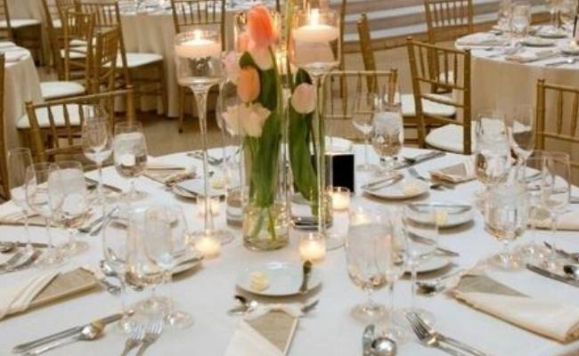 Elegant dining setup at a banquet with round tables, white linens, floral centerpieces, and candlelight.