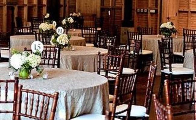 Elegant banquet hall with circular tables covered in white cloths and dark wooden chairs, each table adorned with a floral centerpiece.