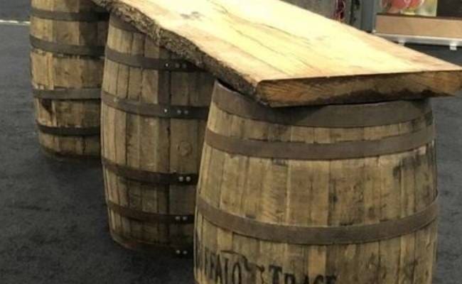 Two wooden barrels repurposed as stands support a natural wood slab countertop in an indoor setting.