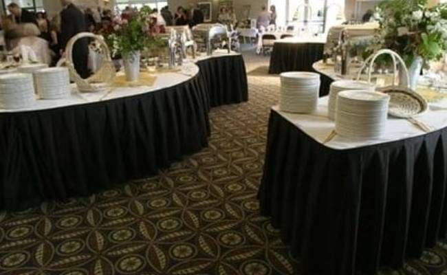 Elegant indoor banquet setting with tables covered in black tablecloths and stacked white plates ready for serving.