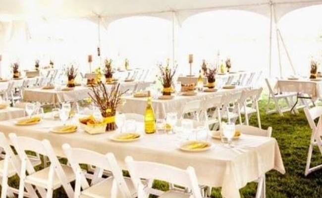 Elegant outdoor wedding reception setup under a white tent with decorated tables, white chairs, and soft lighting.