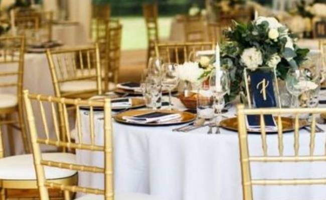 Elegant wedding reception table setting with gold chairs, white floral centerpiece, and navy accents.