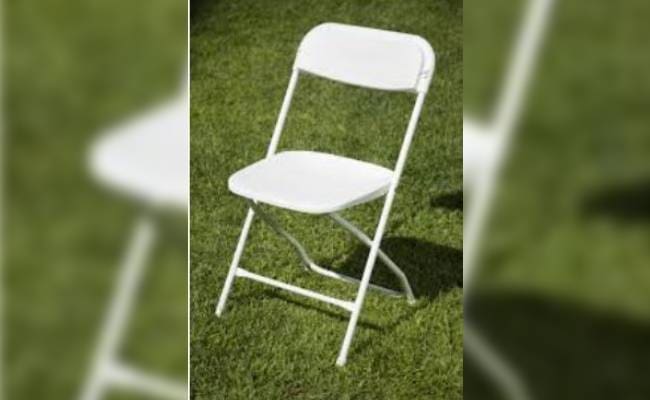 A white folding chair on green grass, slightly out of focus, with partial views of other similar chairs visible.