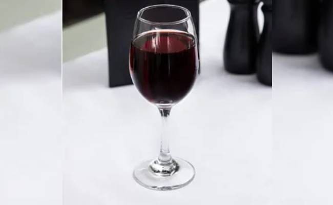 A glass of red wine on a white tablecloth, with a black pitcher partially visible in the background.