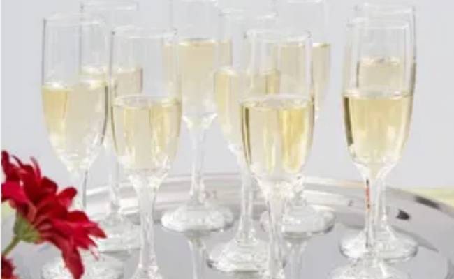 A tray of champagne flutes filled with sparkling wine, partially obscured by a red flower in the foreground.