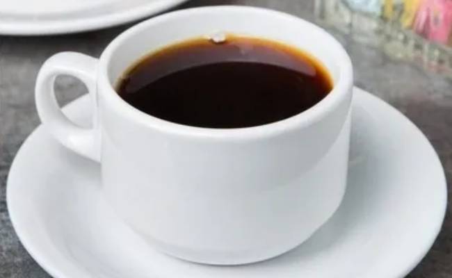 A white ceramic cup filled with black coffee on a matching saucer, placed on a grey table.