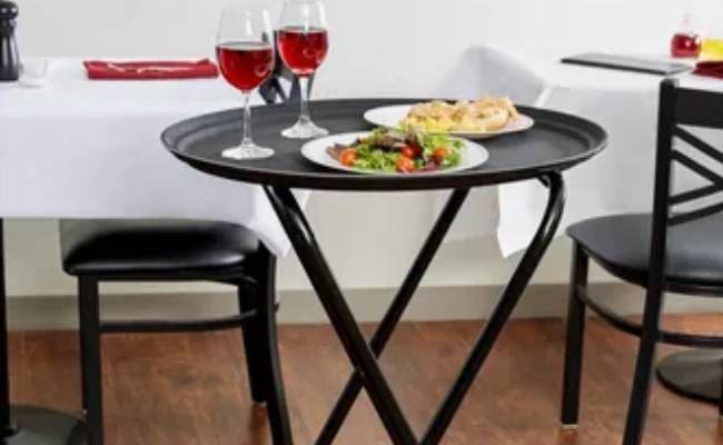 A small round dining table with two plates of food, two glasses of red wine, and a black chair in a modern room setting.