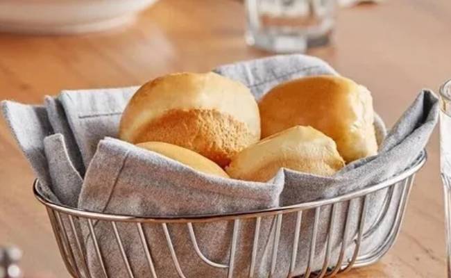 A basket of freshly baked dinner rolls wrapped in a cloth napkin on a wooden table.