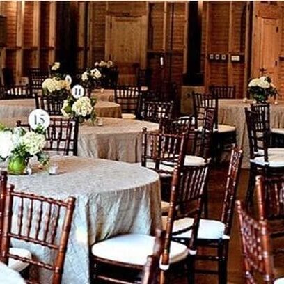 Elegant banquet hall setup with round tables, beige tablecloths, dark wooden chairs, and white floral centerpieces.