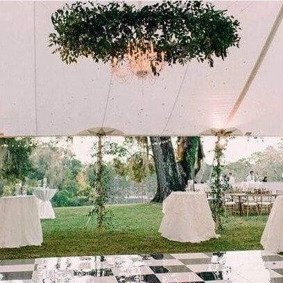 Elegant outdoor wedding reception under a tent with white draped ceilings, hanging greenery, chandeliers, and a checkered dance floor.