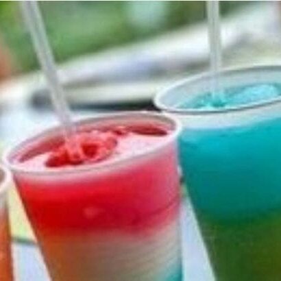 Colorful slushie drinks in red and blue with straws, focusing on the vibrant colors and the frosty texture, set against a blurred outdoor background.