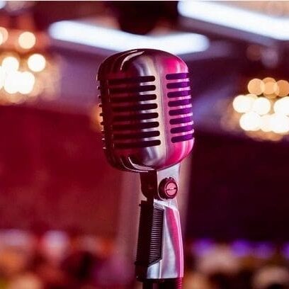 Close-up of a vintage microphone on a stand with a blurred background of a softly lit event hall.