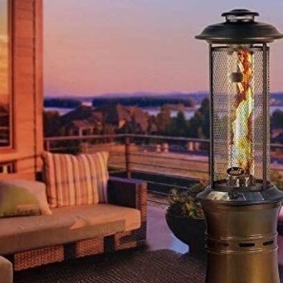 A patio at sunset featuring a glowing outdoor heater, a cozy sofa, and a view of a tranquil lake.